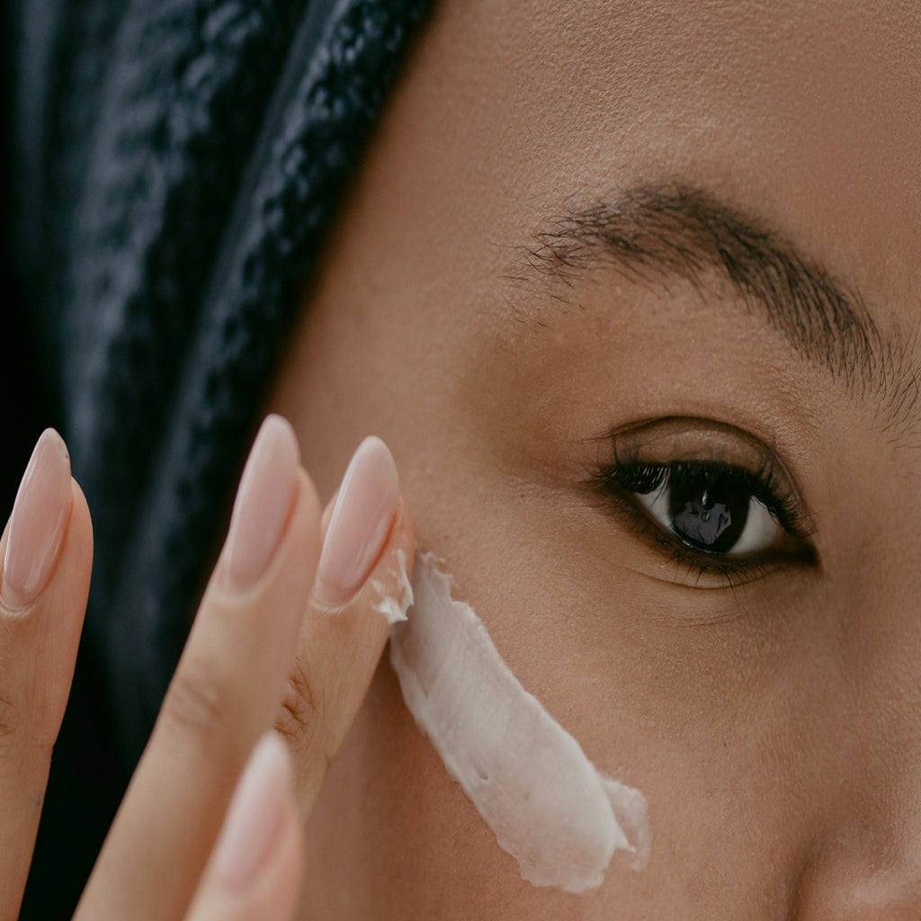 picture of black girl with towel on her head smearing active eye cream under right eye.